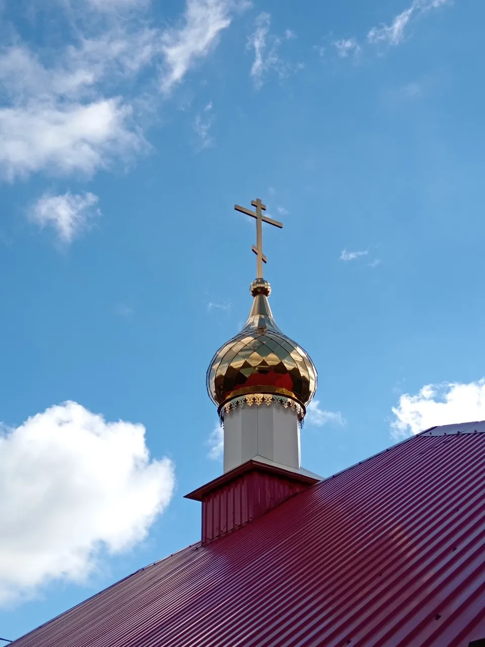 Золотой купол с крестом над красной кровлей на фоне неба